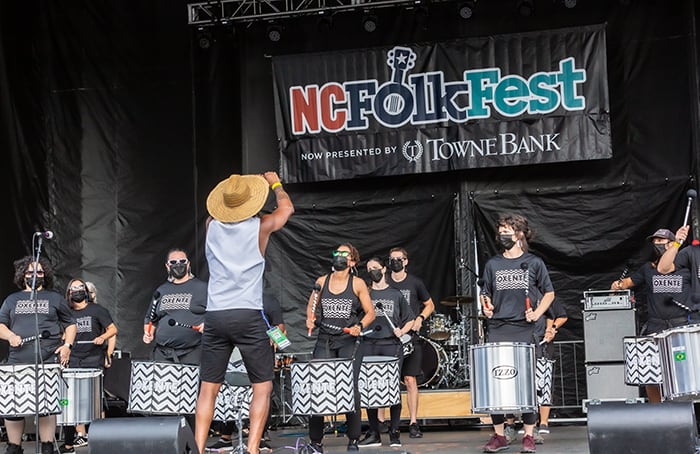 Performers on stages holding a NC Folk Festival sign.