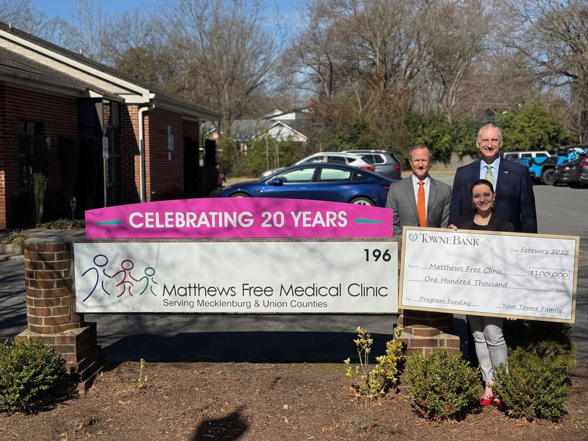 group photo standing beside the matthews free medical clinic sign that has a townebank check