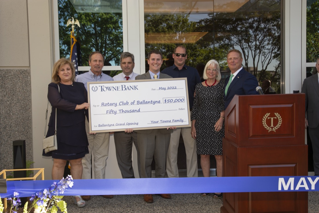 Group of seven people holding a large donation check at a grand opening event.
