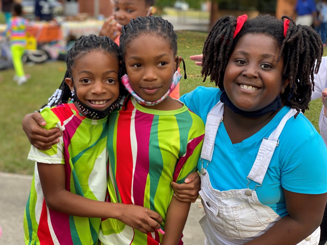 Close up photo of three children embracing.