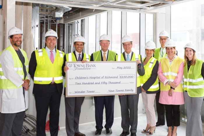 Group of nine people wearing construction hats holding large donation check.