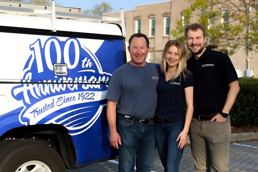 Three smiling people standing next to work truck.