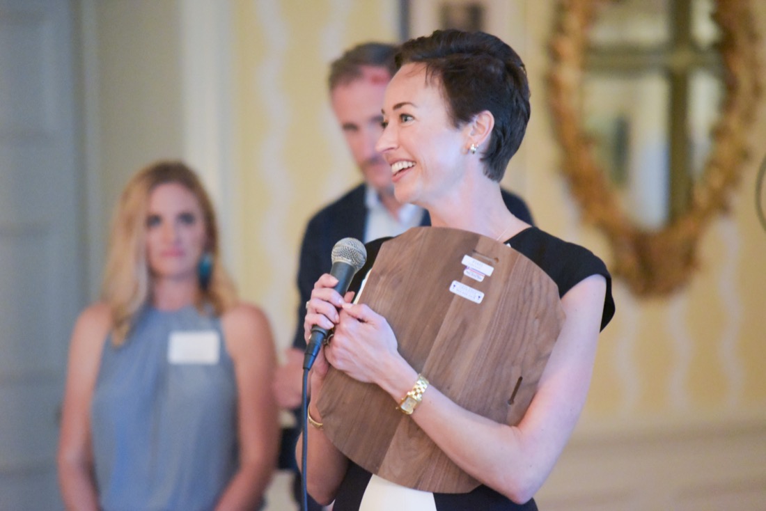 Photo of Tracey Jameson speaking into a microphone while holding an award plaque.