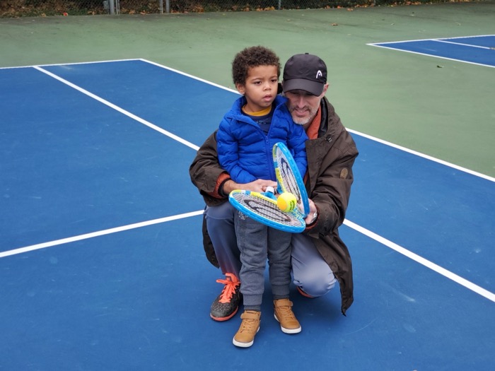 Photo of an adult helping a child hold a tennis racquet.