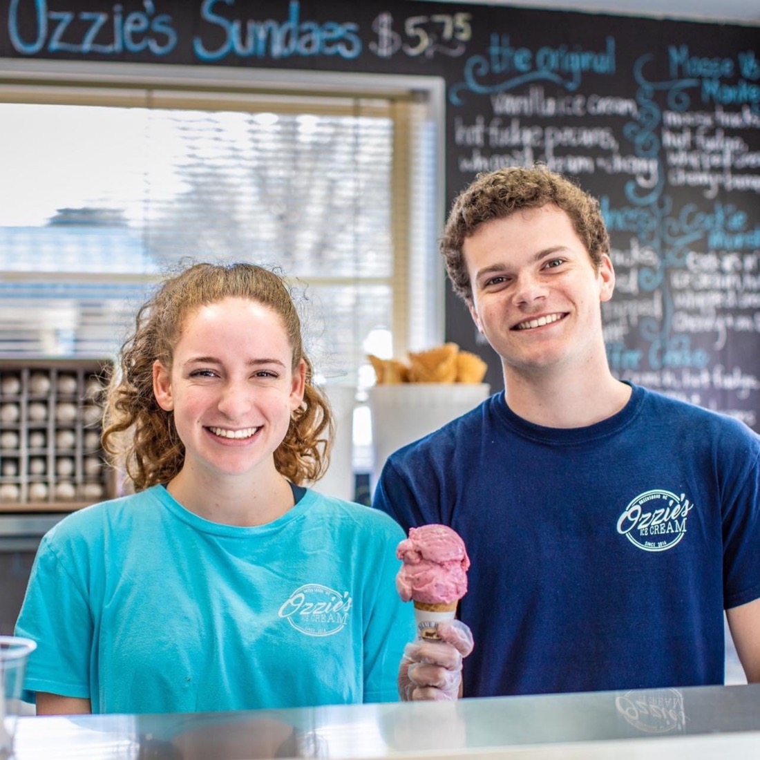 Close up photo of two smiling workers in an ice cream shop.