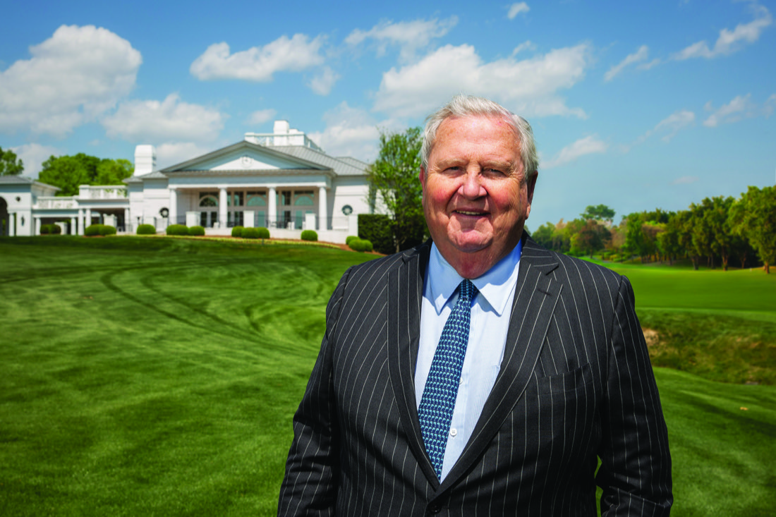 Johnny Harris standing on golf green with clubhouse in the distance behind him.