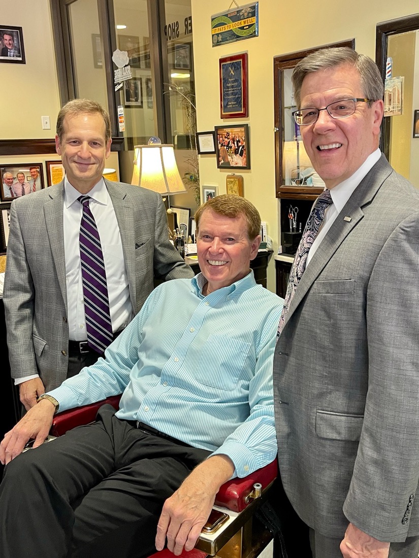 Photo of three people standing at a barbershop chair.