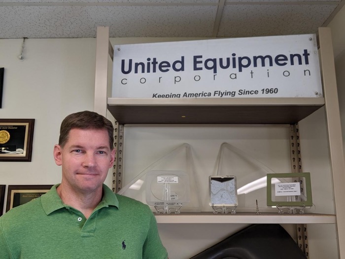 Interior photo of Trace Higgins standing next to company logo sign